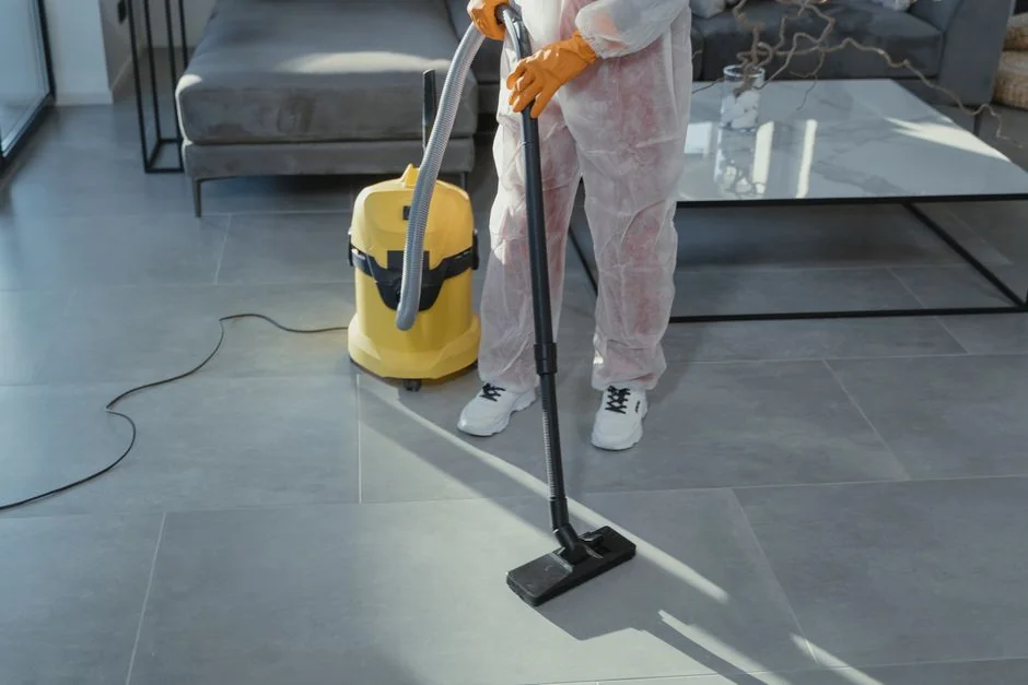 Person in protective gear disinfecting bathroom sink with spray bottle.